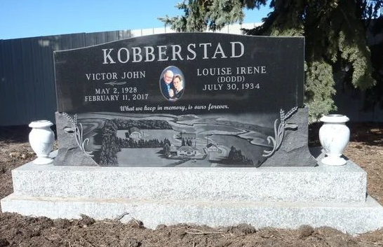 Black granite gravestone marked “KOBBERSTAD,” set on a white base with white urns on both sides.