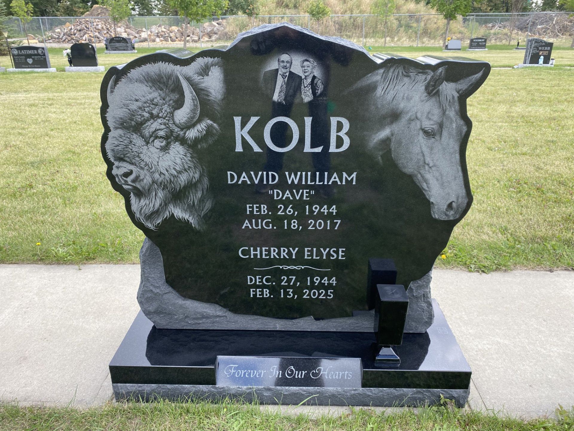 Black granite gravestone for Kolb in a cemetery, with two angel carvings and flower vase.