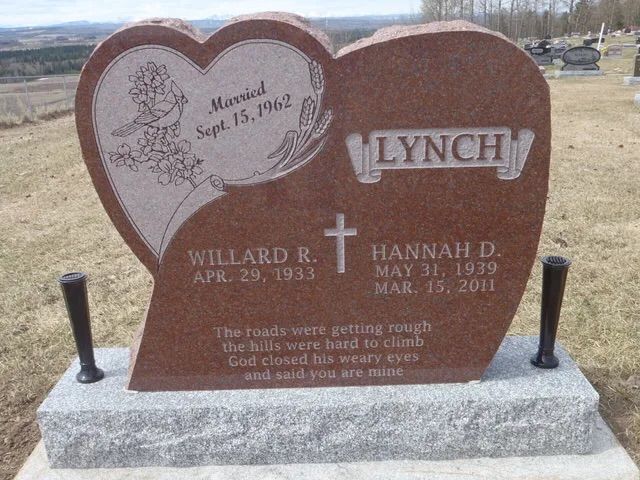 Brown heart-shaped gravestone with engraved names and dates in a cemetery.