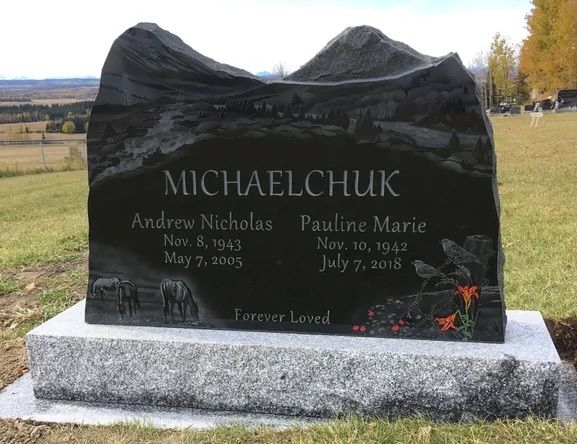 Black granite memorial headstone on a concrete base in a grassy cemetery field with engraved names and dates