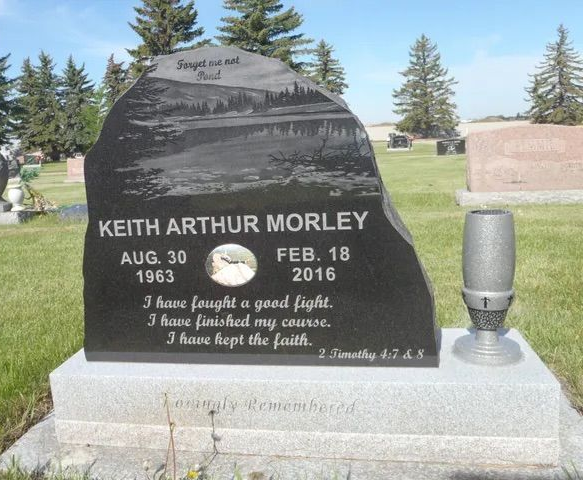 Black gravestone for Keith Arthur Morley in a cemetery, with dates and engraved memorial verse.