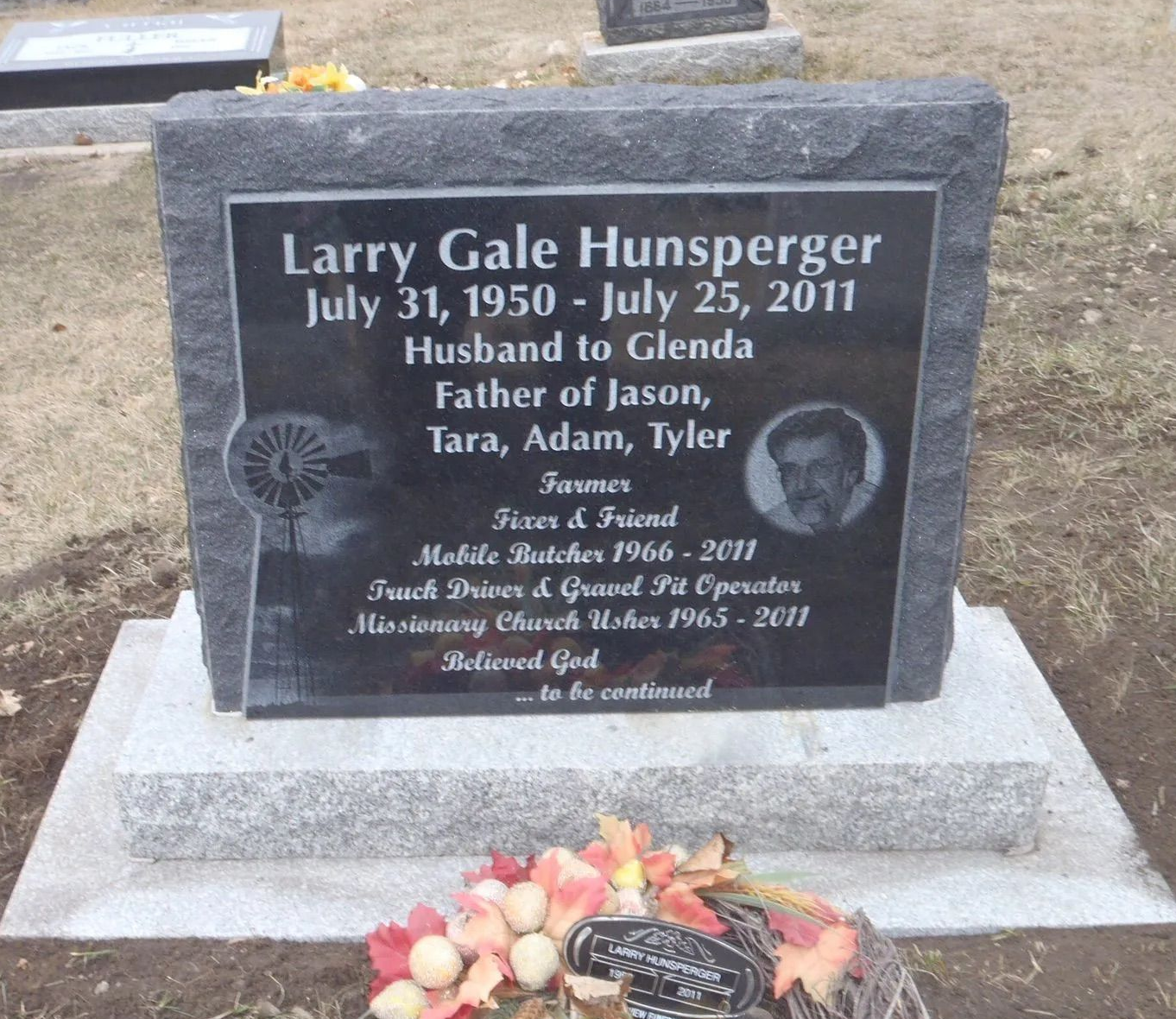 Gray granite memorial headstone with engraved plaque and flowers at the base.