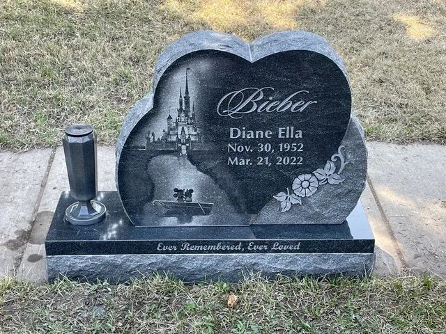 Black memorial gravestone with angel engraving and flowers, engraved for Diane Ella, in a cemetery