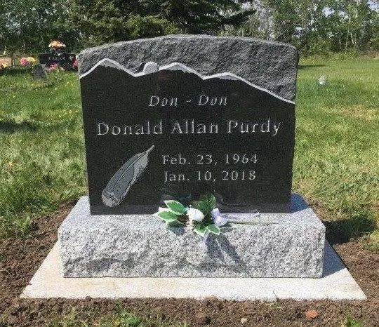 Black granite memorial headstone on a concrete base with flowers in a grassy cemetery.