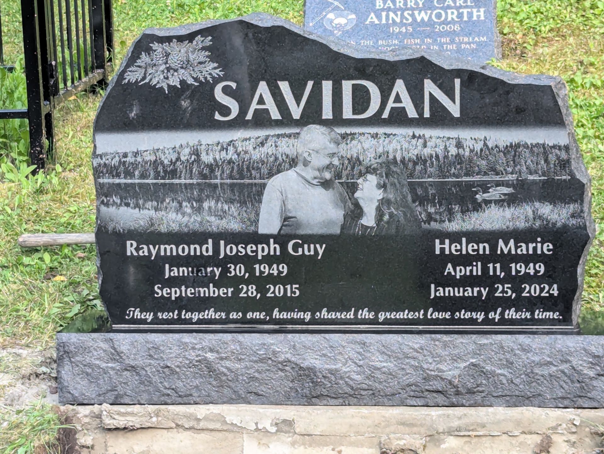 Black granite gravestone with names Raymond Joseph Guy and Helen Marie in a cemetery