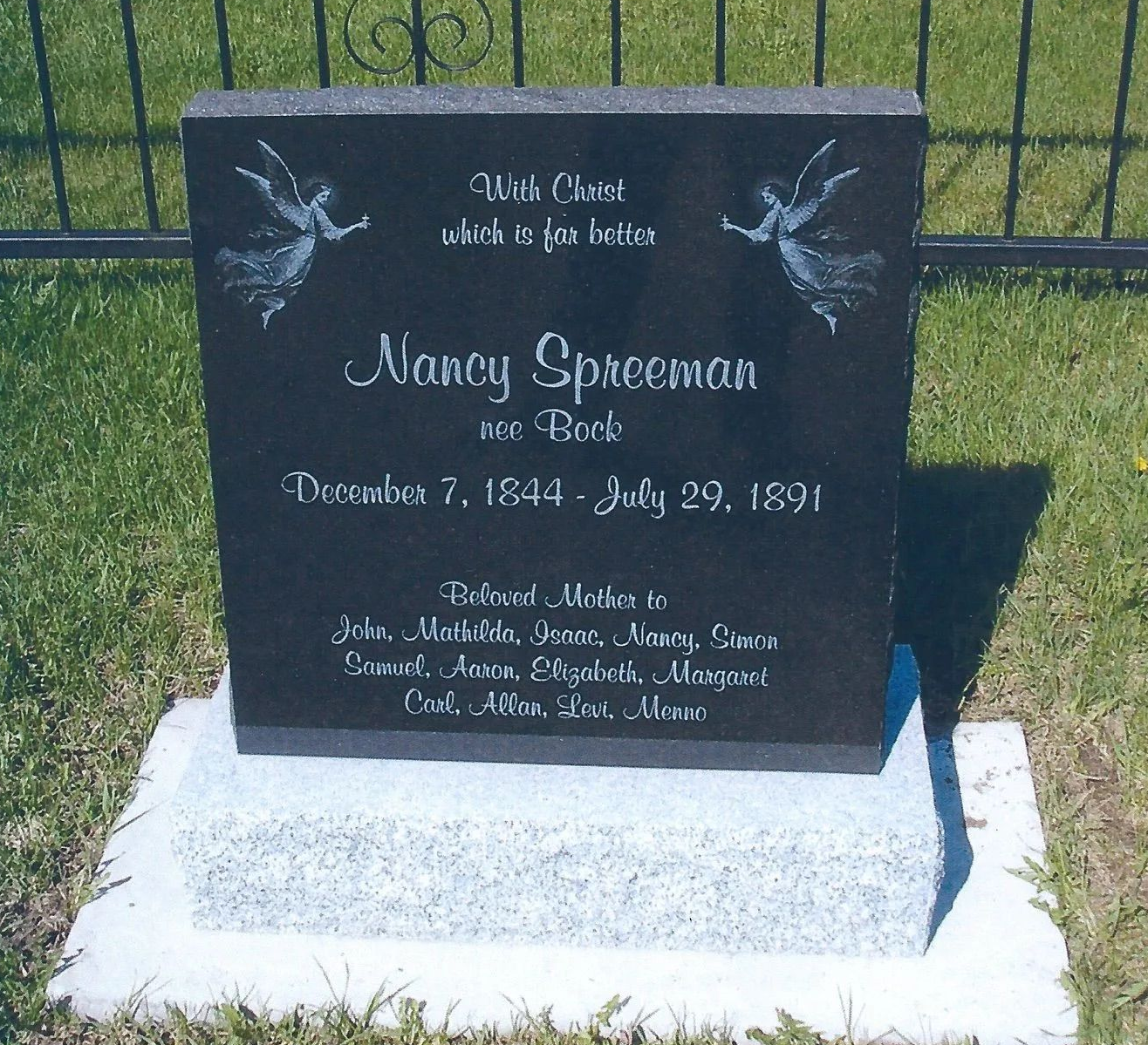 Black gravestone memorial plaque on a white base in a grassy cemetery.