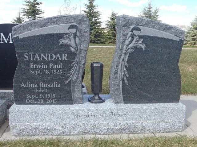 Black granite double gravestone with floral engraving and names in a cemetery lawn