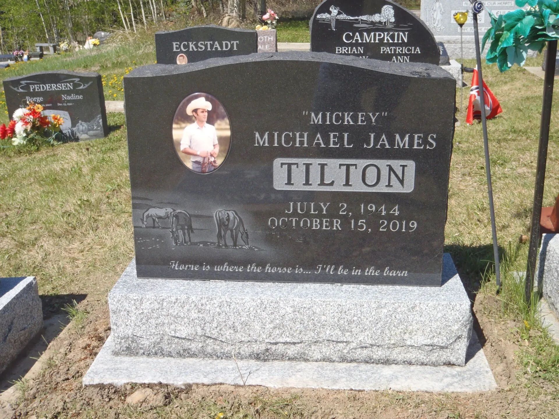 Black granite memorial headstone for Mickey Michael James Tilton with photo and dates in a cemetery