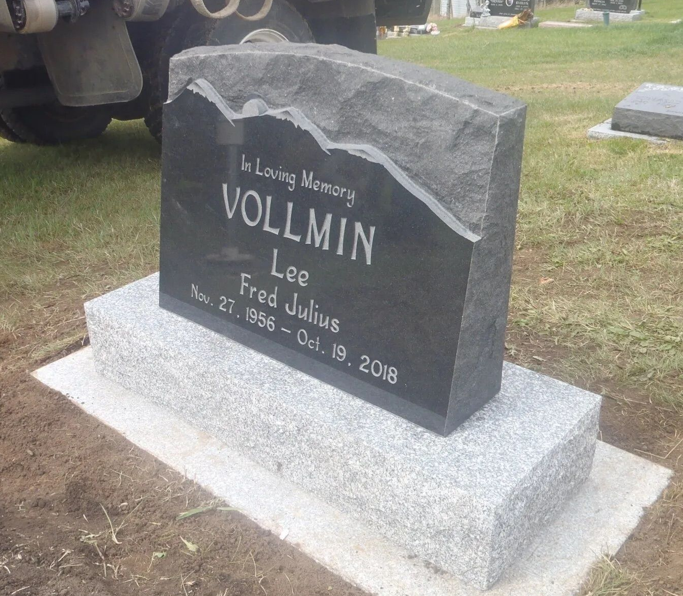 Gravestone in a grassy cemetery, black stone on a gray base, engraved “VOLLMIN” and “Lee.”