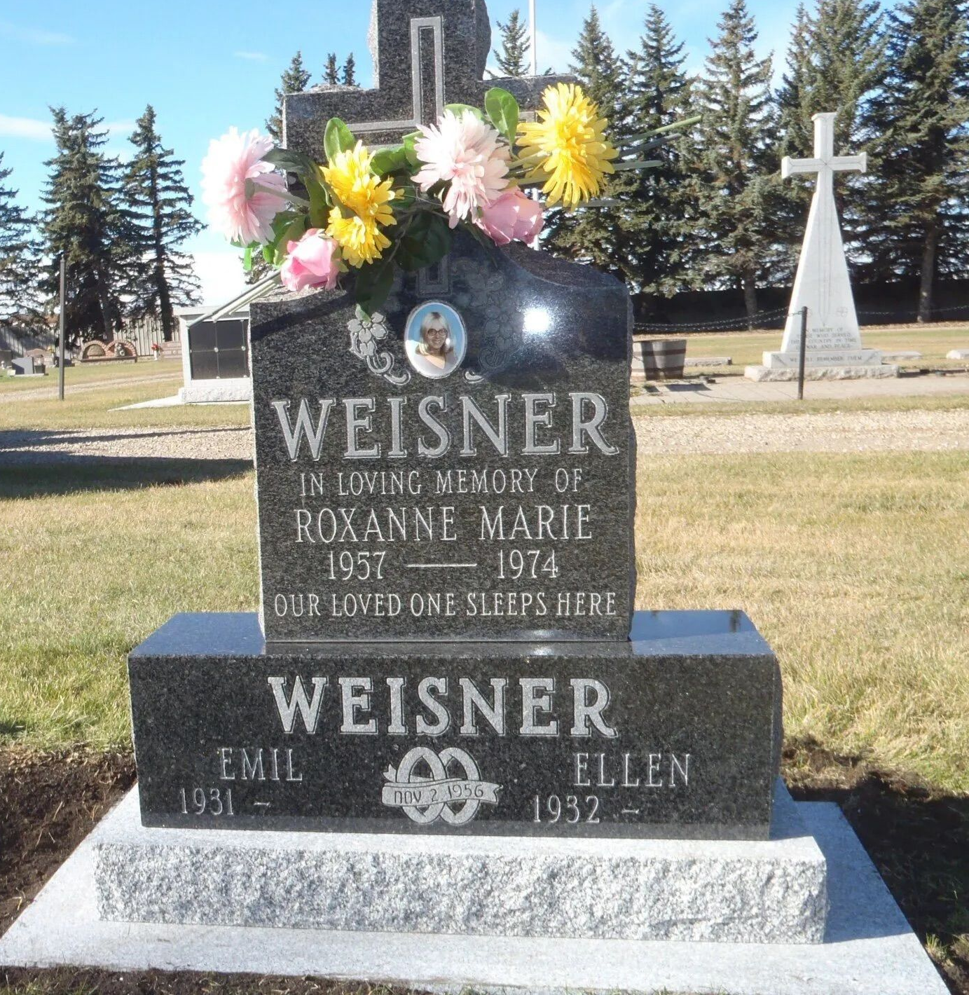 Weisner family gravestone with flowers in a cemetery, featuring a black marker and cross monument.