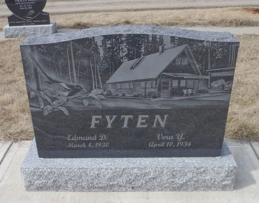 Black granite gravestone with engraved cabin scene and the name “FYTEN” in a cemetery.