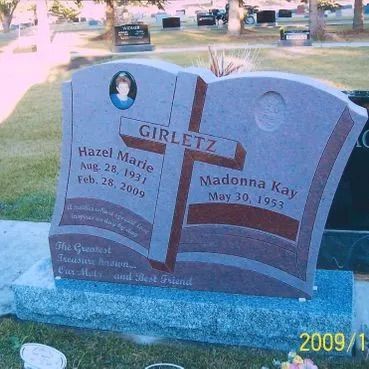 Gray double gravestone with a red cross in a grassy cemetery, engraved “GIRLEZ.”