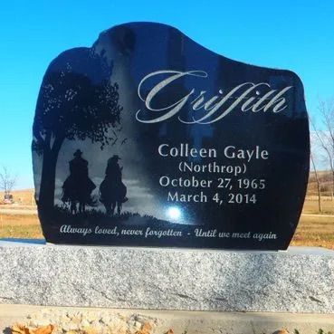 Black granite memorial headstone with engraved names and dates against a blue sky