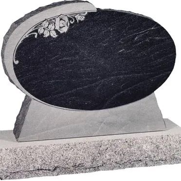 Black oval gravestone with floral carving on a light stone base, set on a grave site.