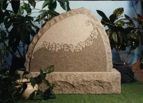 Decorative granite memorial stone with engraved floral border, set in a garden with plants behind it