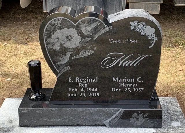 Heart-shaped black granite gravestone with floral engraving for Hall and two names at a cemetery.