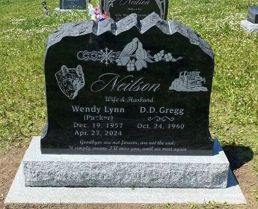 Black granite gravestone with floral etching and the name “Nelson” in a cemetery