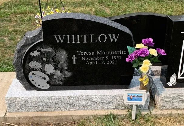 Black granite gravestone with “WHITLOW” and flowers placed beside it in a cemetery.