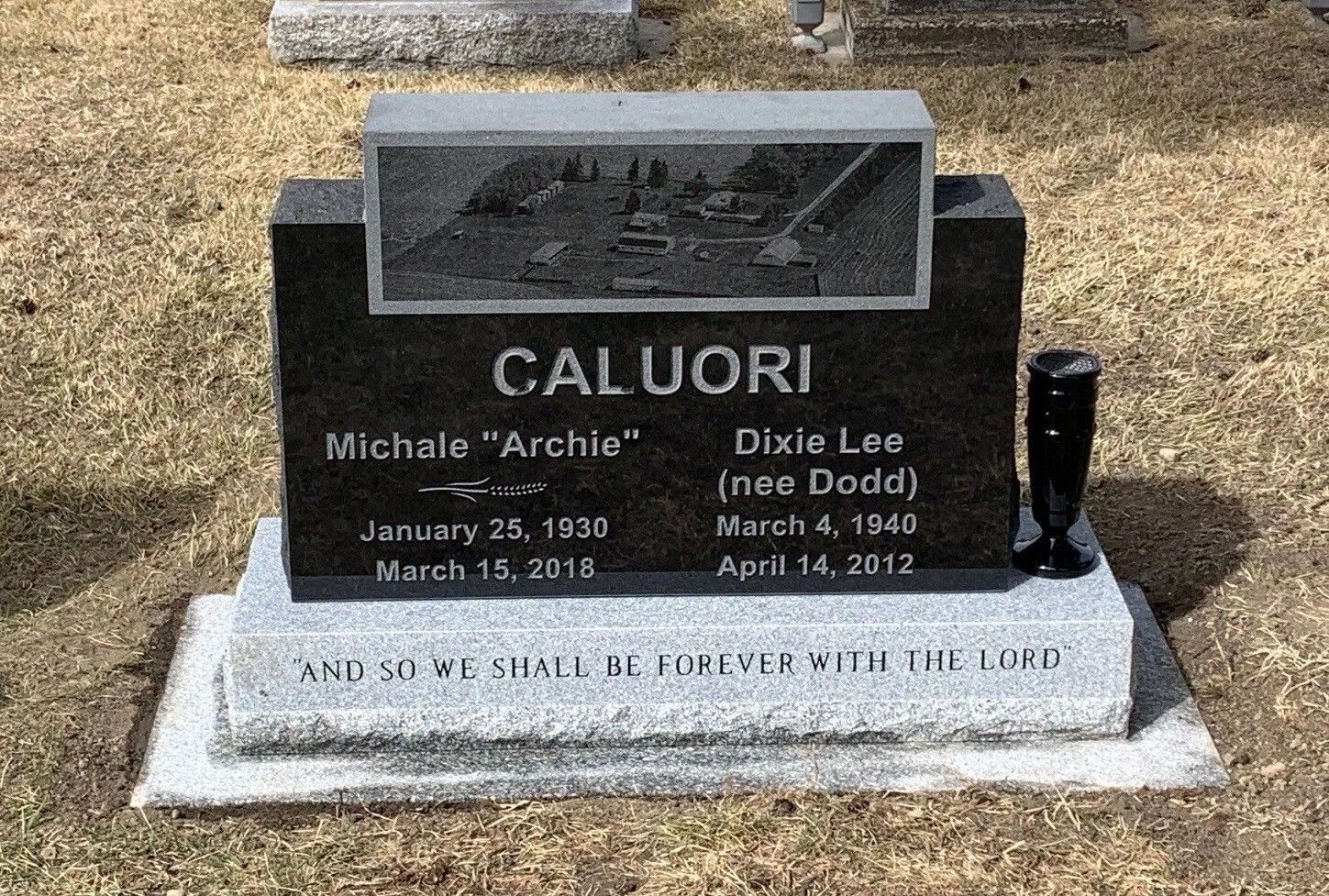 Black Calori memorial headstone with engraved names and dates on a cemetery lawn