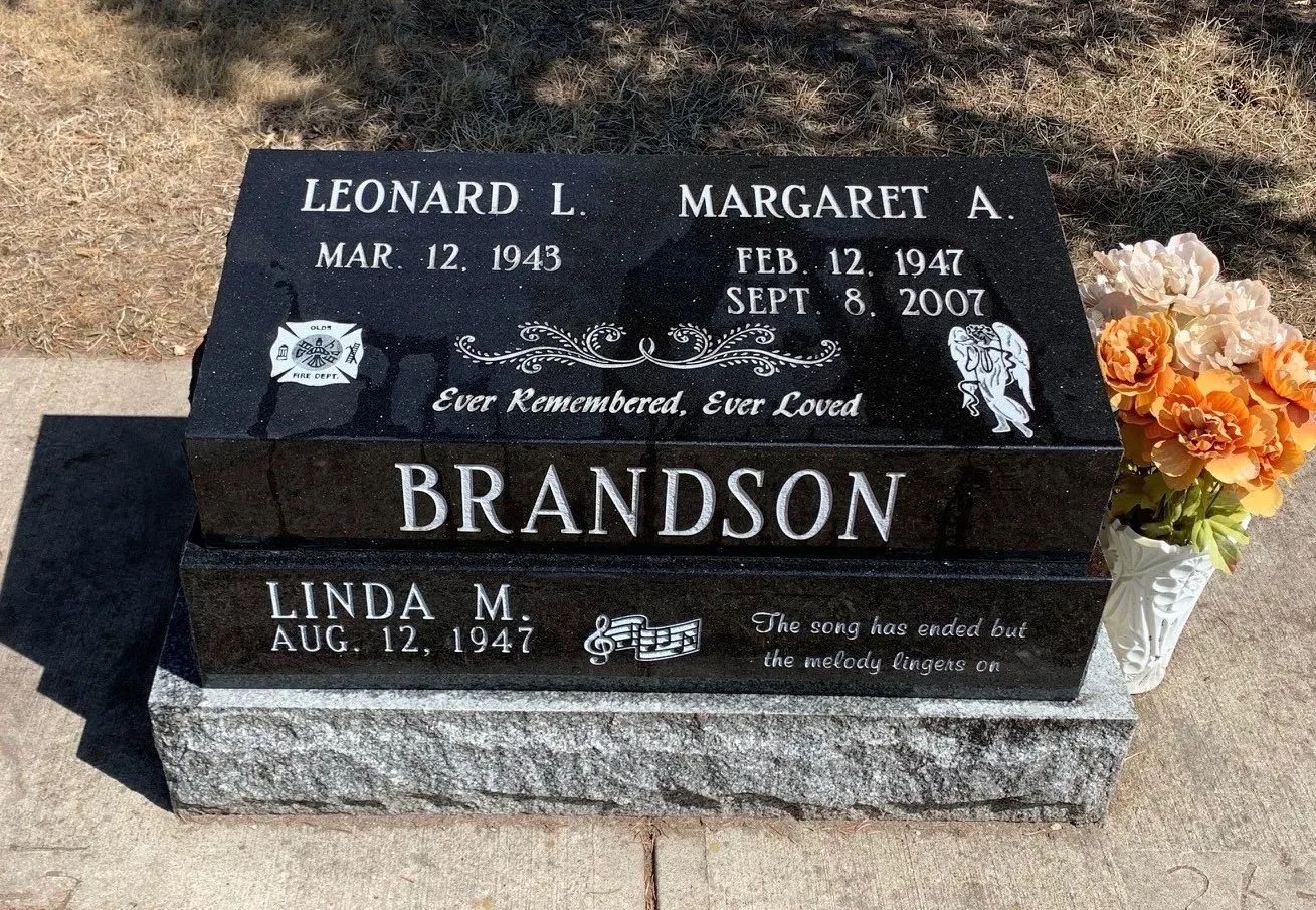 Black granite grave marker for Leonard L. and Linda M. Brandson with flowers beside it.