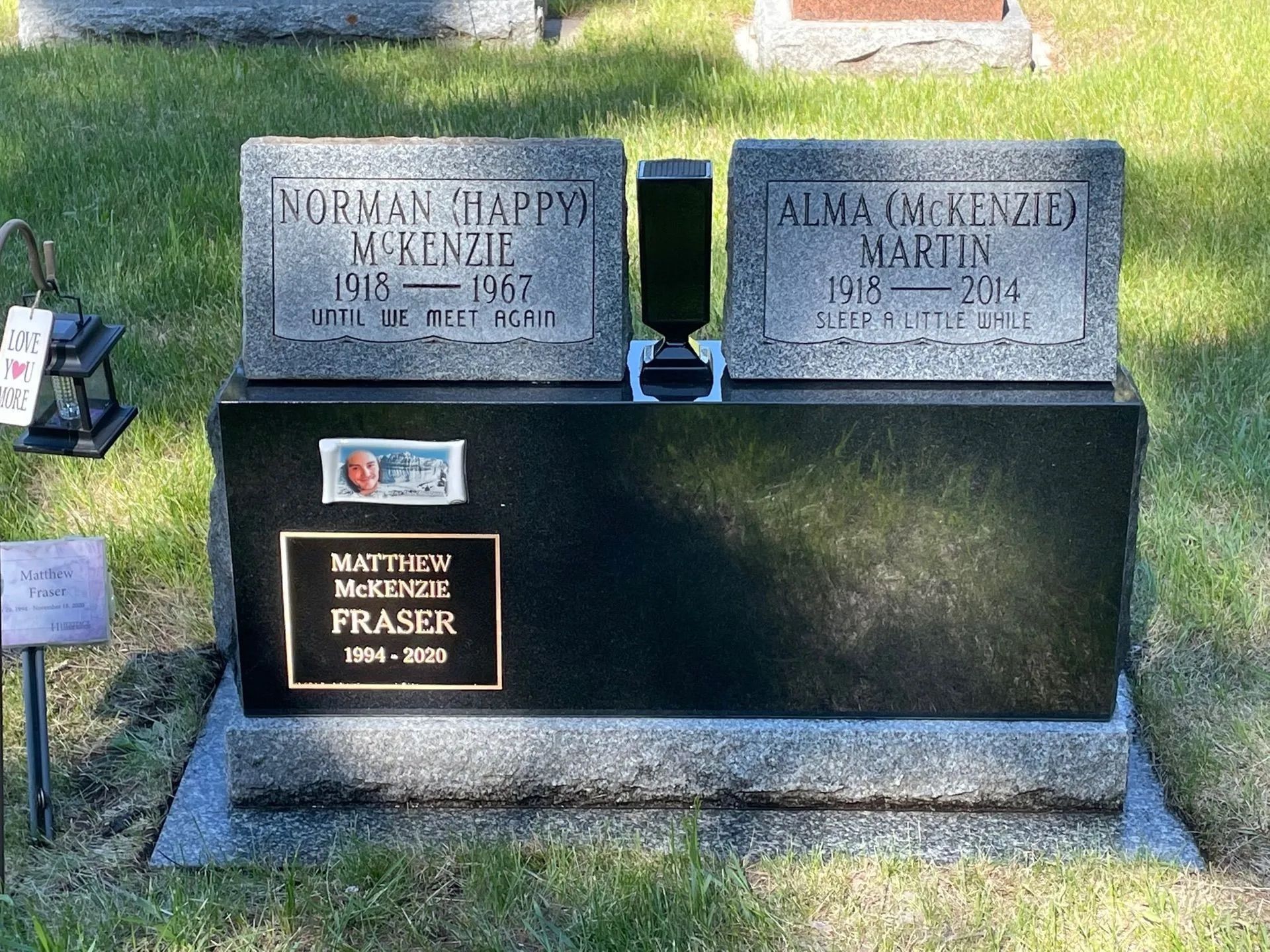 Gravestone with two gray headstones on a black base in a grassy cemetery area
