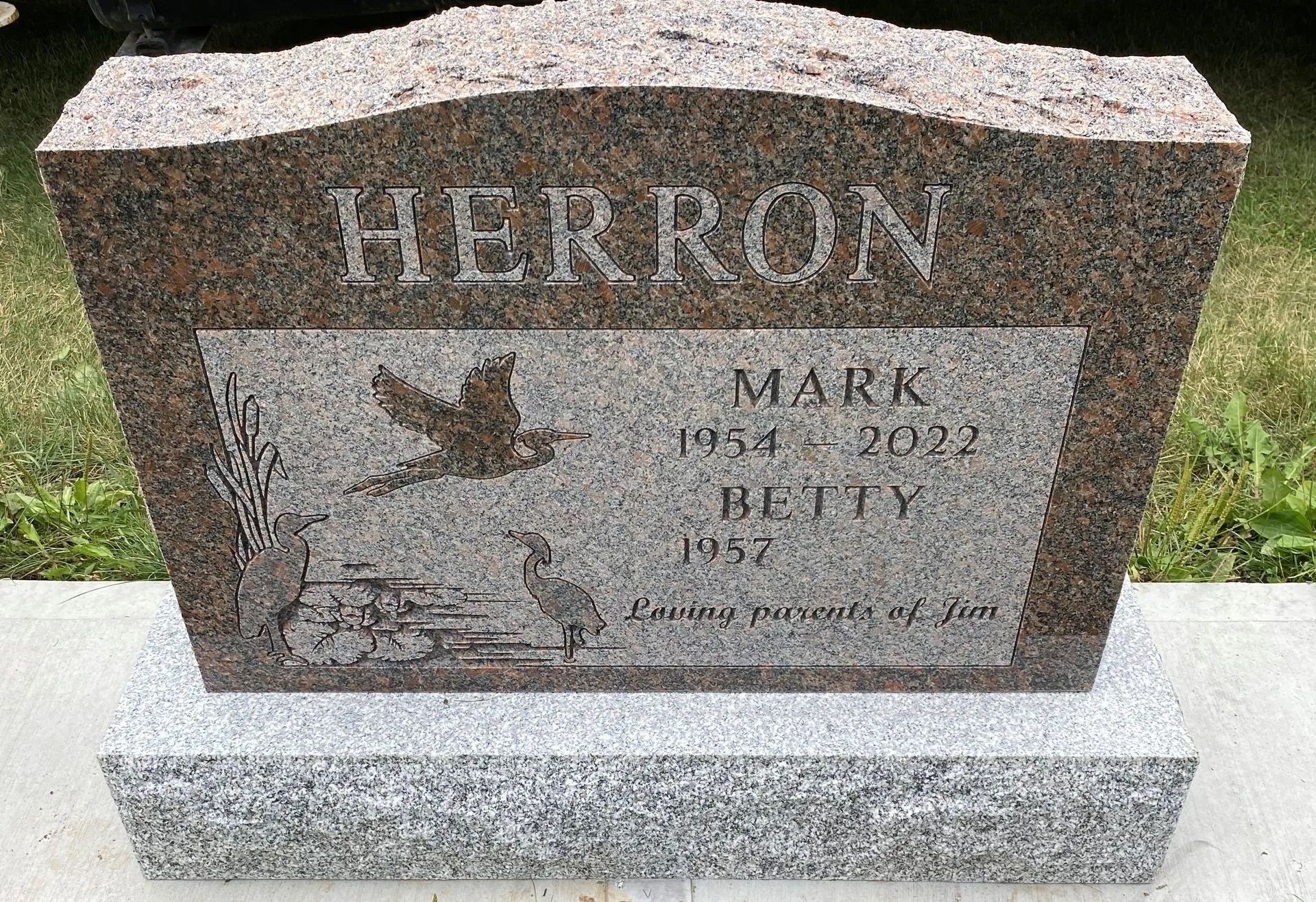 Gray granite gravestone with the name HERRON and engraved maple leaf, set on a white base.