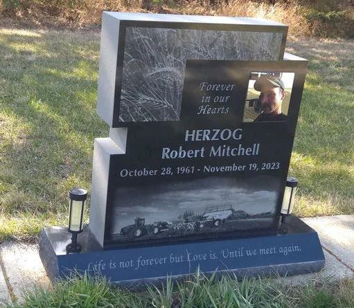 Gravestone memorial with photo and plaque, reading “HEROIC Robert Mitchell,” in a grassy cemetery setting