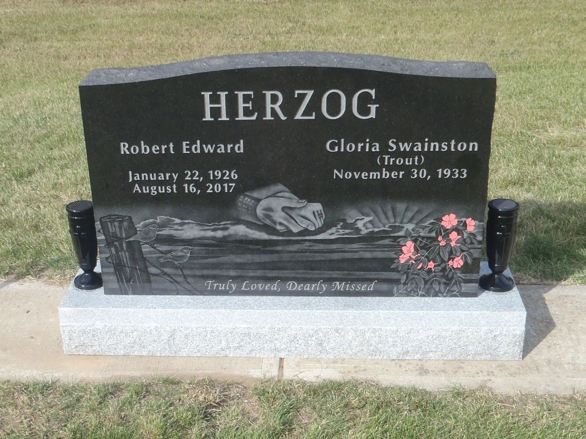 Black gravestone with “HERZOG” and pink flowers on a cemetery lawn
