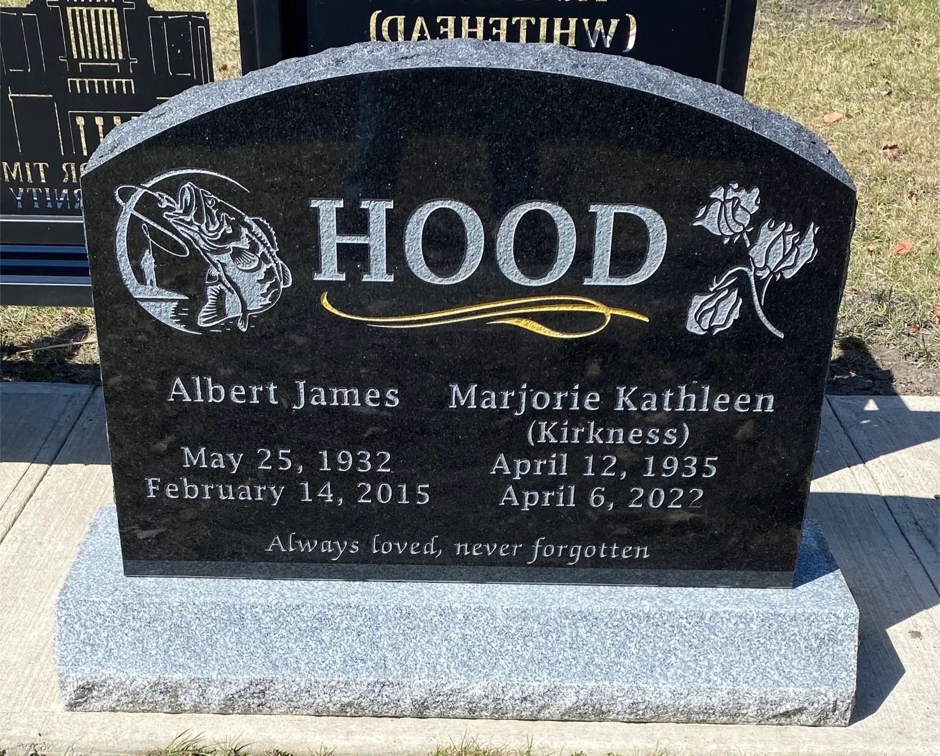 Black granite gravestone engraved “HOOD” with two names and dates, set on a light stone base.