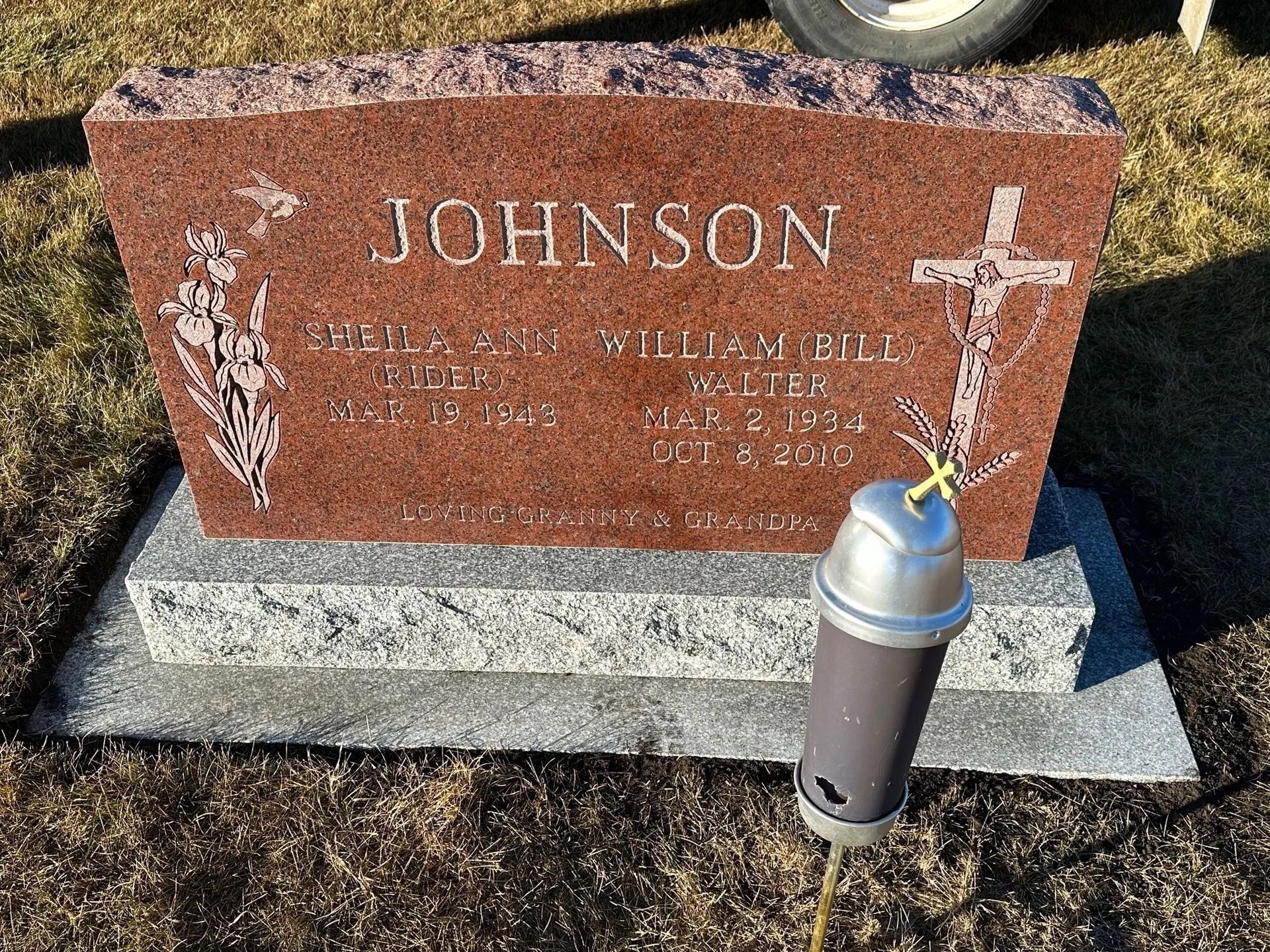 Red granite gravestone marked “JOHNSON” with a cross, on a gray base outdoors.