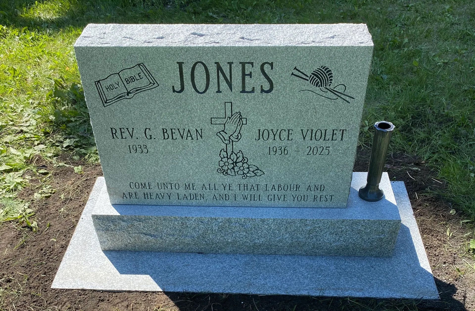 Gray granite gravestone with “JONES” engraved, set on a white base in a grassy cemetery plot