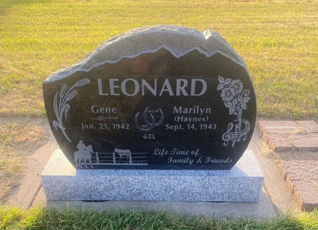 Leonard family gravestone on a gray base in a grassy cemetery, with floral engravings and two names.