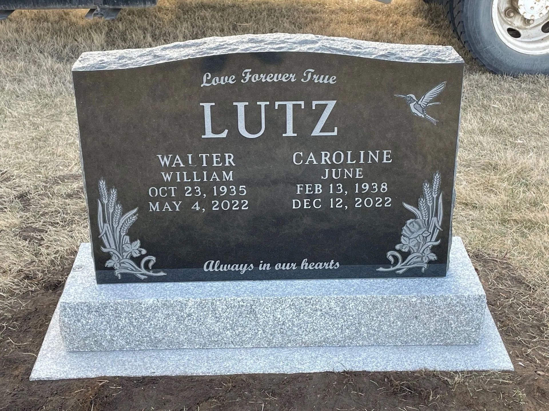 Black granite memorial headstone with flowers and names Walter and Caroline Lutz engraved on it