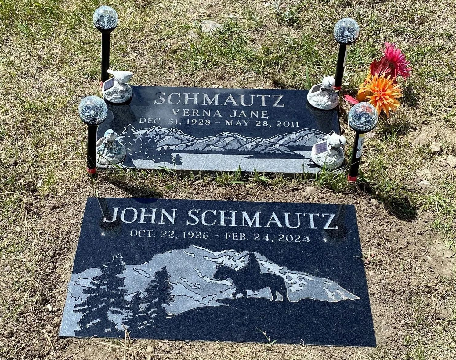 Two black stone memorial plaques with inscriptions and mountain landscape engravings, decorated with pink flowers