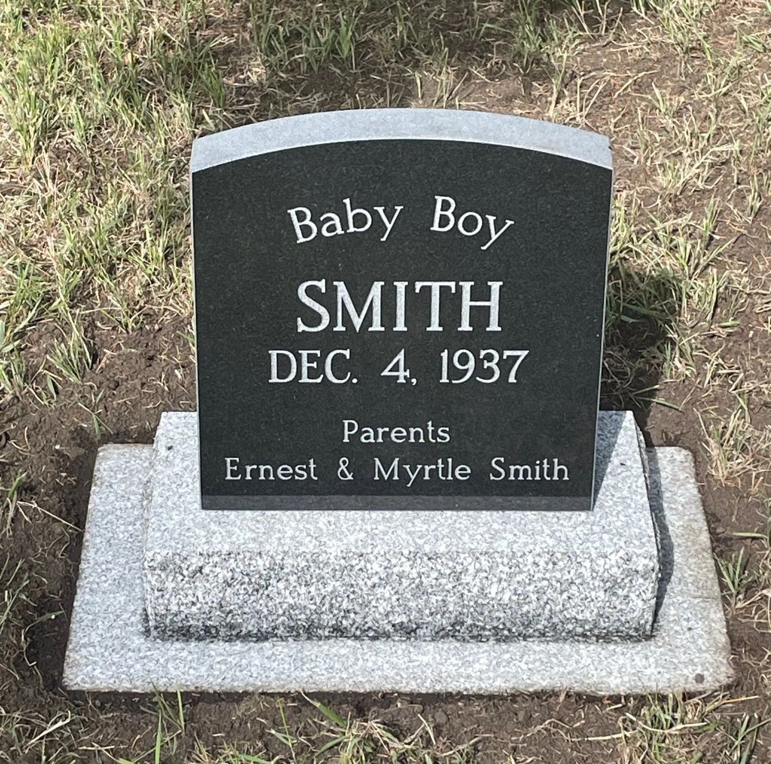 Black granite baby grave marker reading “Baby Boy Smith, Dec. 4, 1937” on a gray stone base.