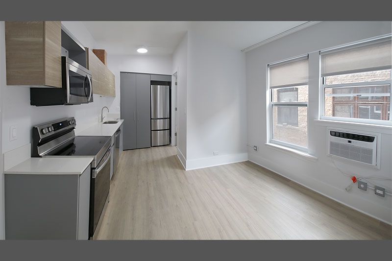 A kitchen with a stove , refrigerator , microwave and a window.