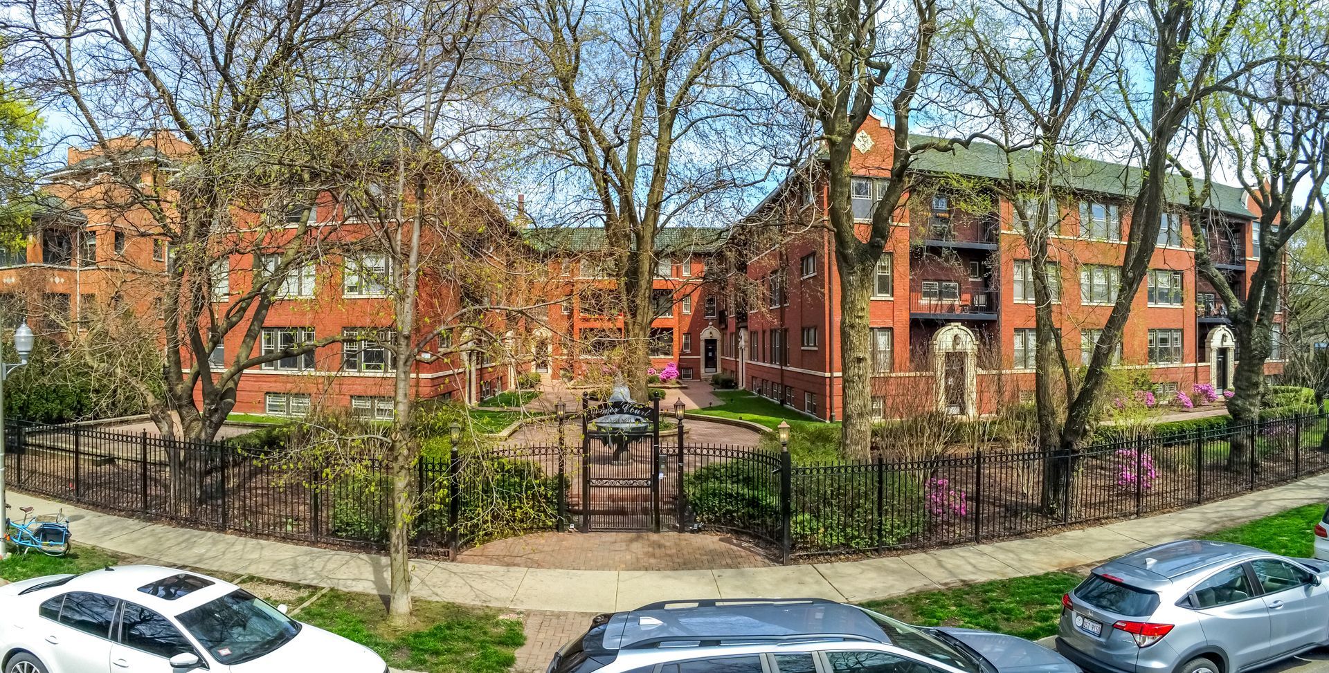 A panoramic view of a brick apartment building with cars parked in front of it.