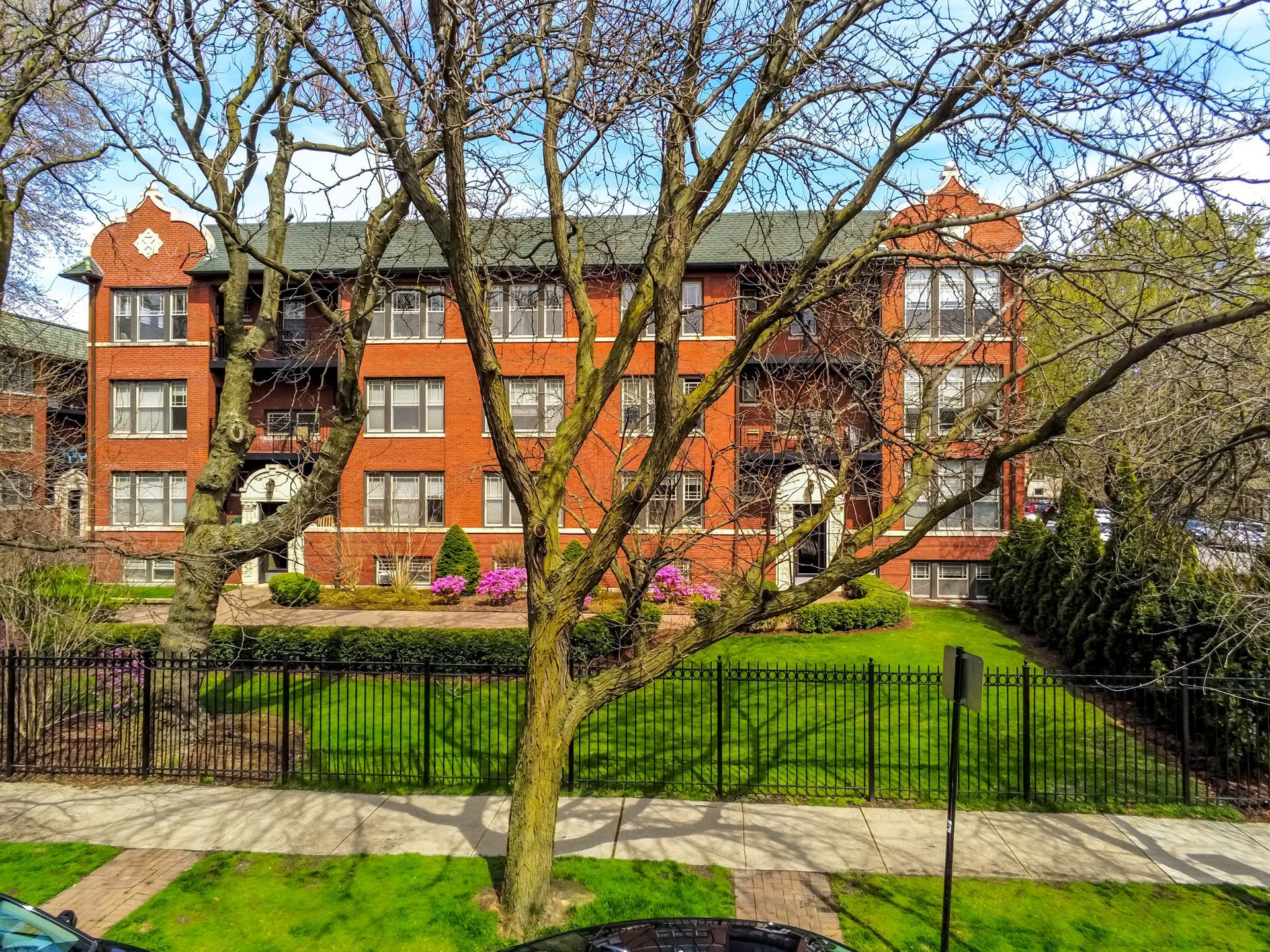 A large brick apartment building with a fence around it and a tree in front of it.