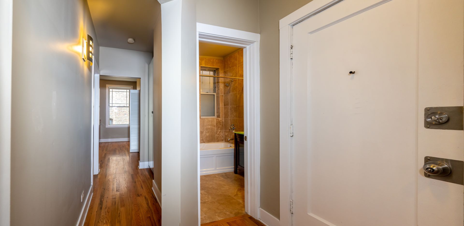 A hallway with hardwood floors and a white door leading to a bathroom.