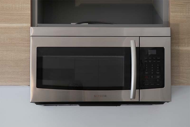 A stainless steel microwave oven is mounted on a wall in a kitchen.