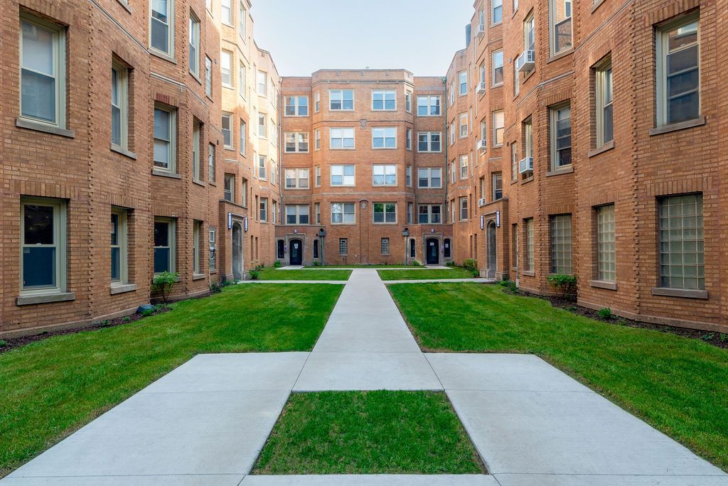A large brick apartment building with a lush green courtyard in the middle.