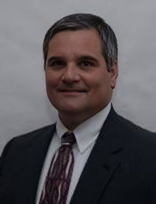 Portrait of a man in a dark suit and patterned tie against a gray background