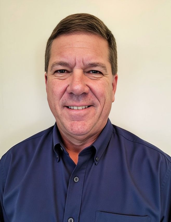 Smiling person in a dark blue button-up shirt against a plain light background