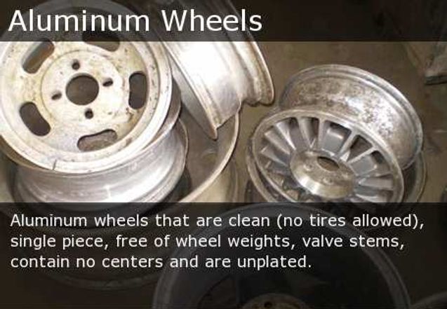 Stack of used aluminum car wheels and rims, some dirty and worn, labeled “Aluminum Wheels.”