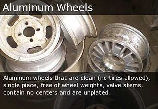 Scrap aluminum wheels, clean and unlabeled, piled together on a dark background
