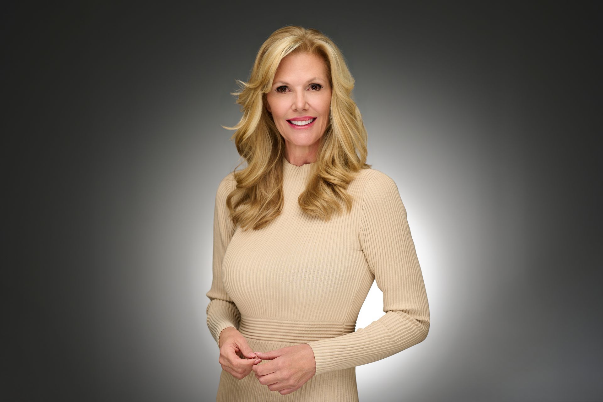 Smiling woman in a beige sweater dress standing against a gray gradient background
