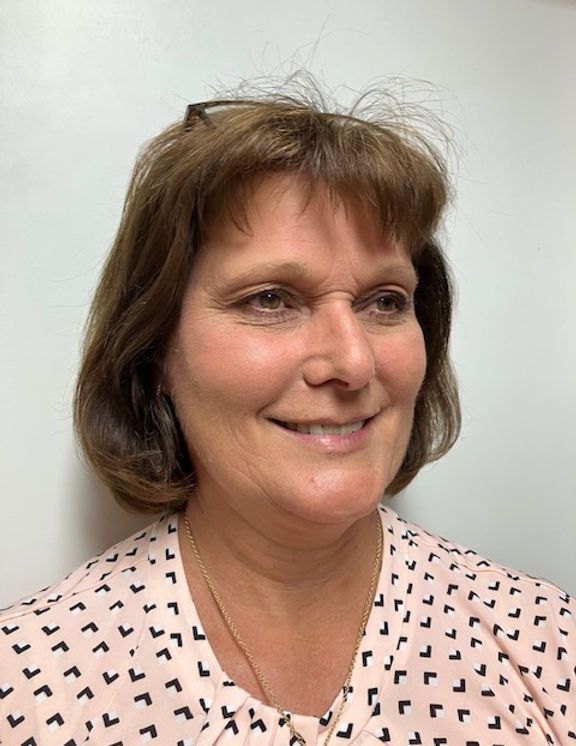 Smiling person in a pink patterned blouse against a plain light gray background