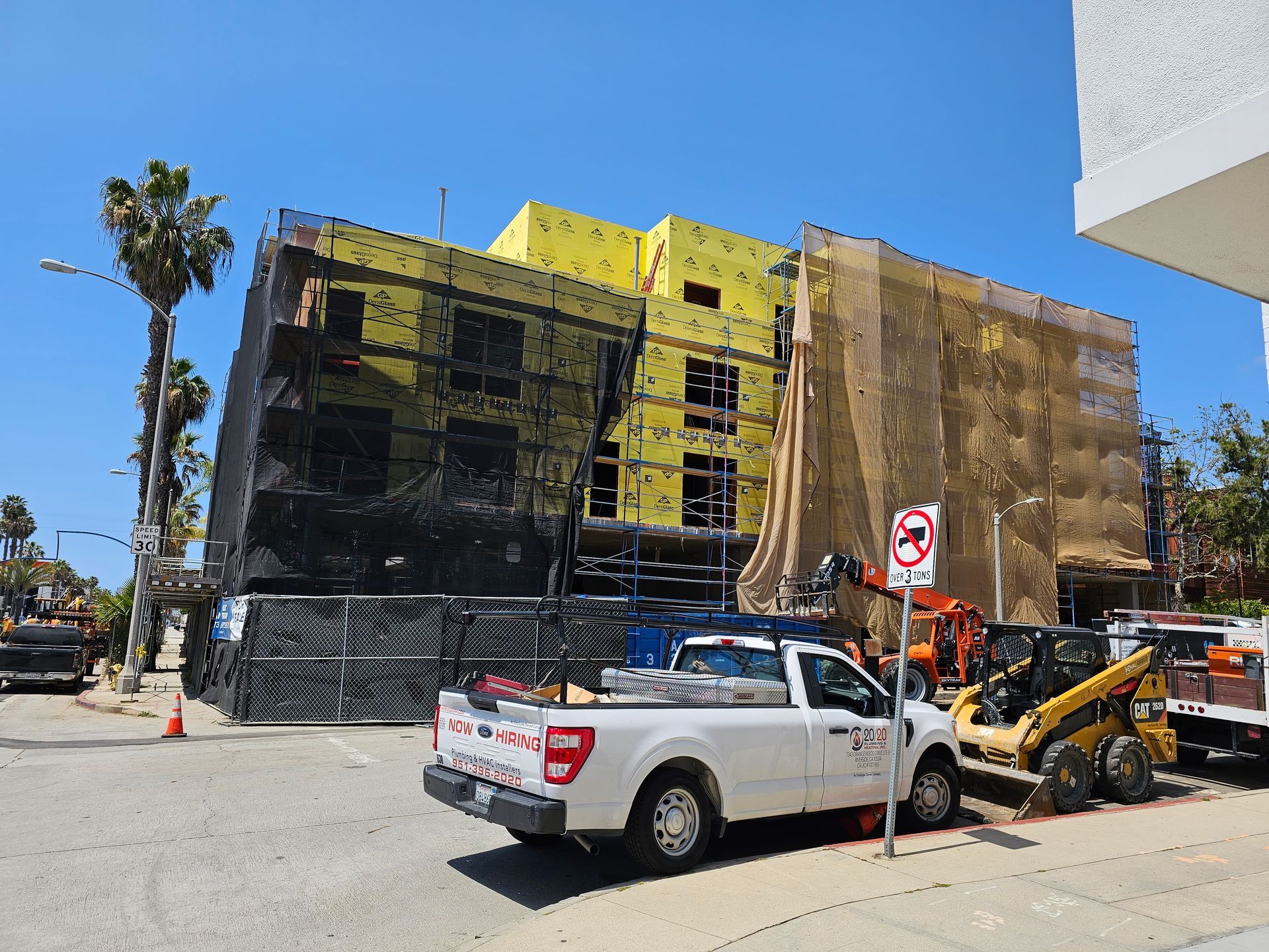 Street view of a yellow building under renovation with construction vehicles and a white pickup truck in front