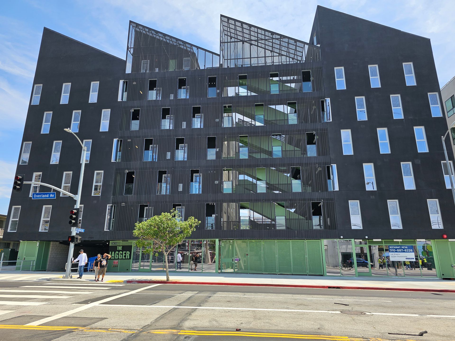 Modern black office building with glass stairwell, street corner, and a few pedestrians outside
