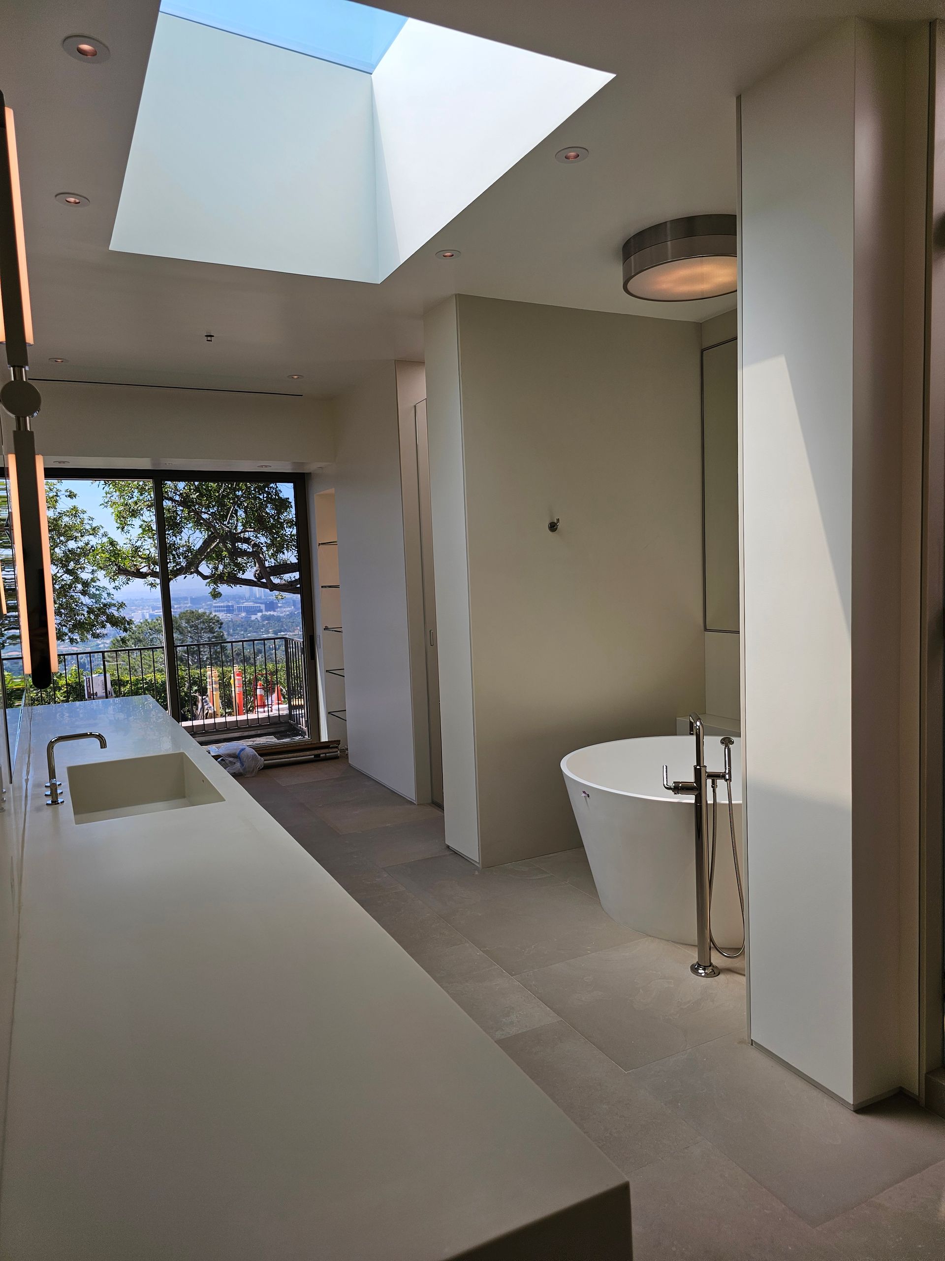 Bright modern bathroom with skylight, long sink counter, and open view to trees outside